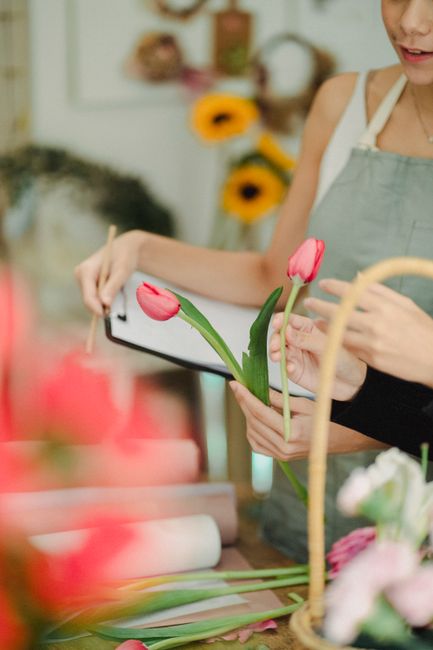 A florist at Kenton Floral Boutique arranging a bouquet of pink tulips with smooth, vibrant petals and green stems, holding them in one hand while preparing to add them to a floral display. The floris