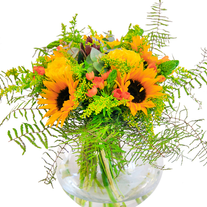 The first impression is pure sunlit energy-the kind that spills through Kenton's leafy avenues on a late August afternoon. This abundant bouquet, arranged in a round, crystal-clear glass vase, features magnificent sunflowers, their faces turned outward and petals rippling in glowing shades of yellow and orange, reminiscent of the golden hour over Kenton Recreation Ground. Among them, clusters of yellow garden roses bloom with classic poise, their tightly packed petals curling into elegant, soft spirals. Scarlet-red hypericum berries gleam between the blossoms, introducing lively sparks of colour that play off the warmth of the sunflowers. The entire piece is woven through with a variety of fresh, verdant greens-cascading fern fronds, airy light-green solidago with clusters of tiny yellow blooms, and slender flower spikes that lift the arrangement skyward. Subtle touches of bluish-green eucalyptus peek out at the edges, enhancing the rustic, locally inspired feel of the bouquet. The glass vase, reminiscent of the fishbowls found on windowsills throughout Kenton, reveals the stems submerged in clear water, adding a serene sense of depth and grounding. This bouquet evokes the joy of local festivals, garden parties, and heartfelt celebrations-its scent a gentle blend of green freshness and floral sweetness. Whether gifted for a birthday, to commemorate an anniversary, or simply to brighten a home near Uxendon Hill, this meticulously handcrafted arrangement is a tribute to happiness and the vibrant life of Kenton.